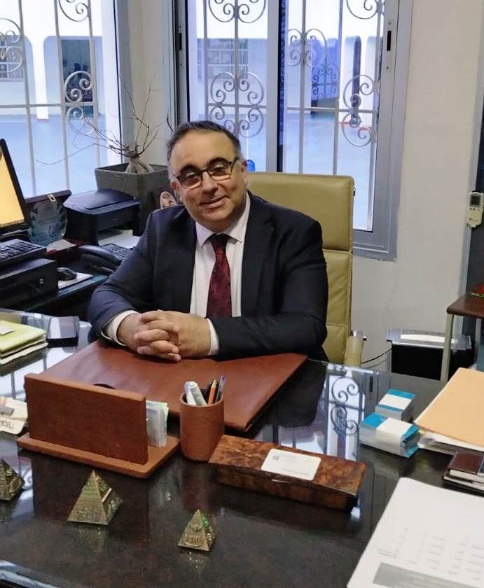 Le Dr Mohamed Chraïbi, Directeur, assis à son bureau, costume sombre et cravate bordeaux.