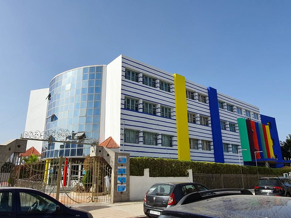 La façade de l'école aujourd'hui : une tour vitrée bleue et un bâtiment blanc rythmé de bandes verticales bleue, jaune, rouge et verte.
