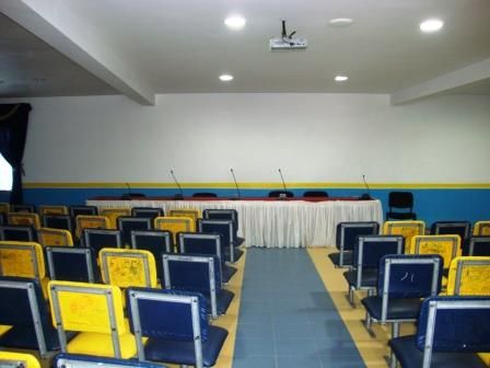 La salle de conférence et ses rangées de fauteuils bleus et jaunes.