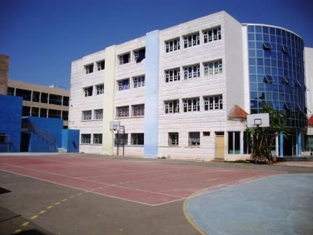 Le terrain de sport et ses paniers de basket, devant un bâtiment de l'école et sa tour vitrée.